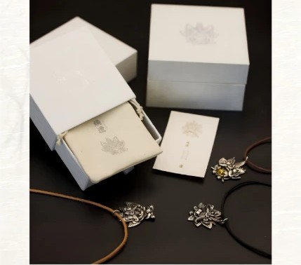 White gift box with the pendant, a meaning card and two cords laid out beside it