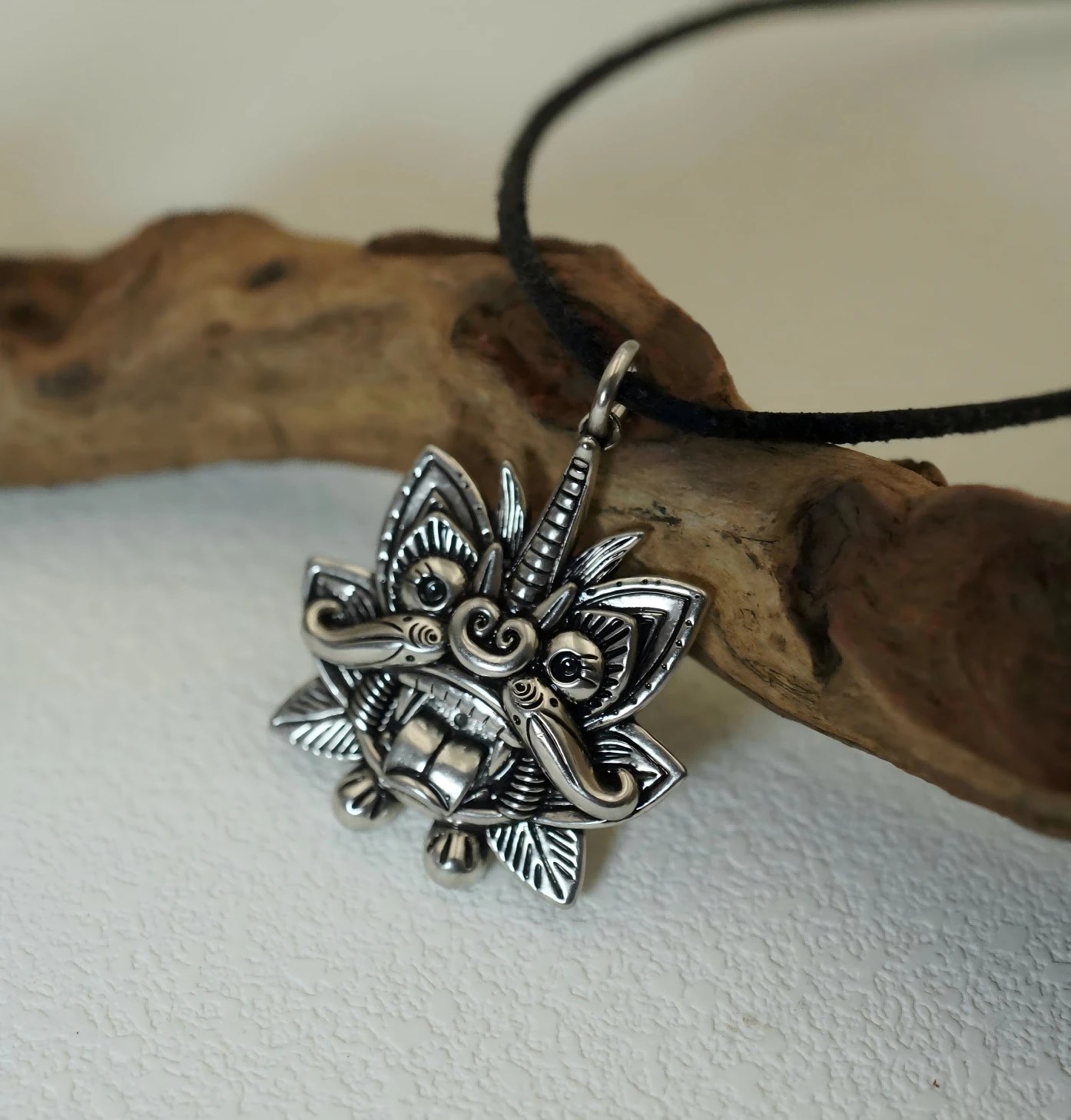 Cangyan silver pendant, a horned roof cat with fangs, on a black cord against driftwood